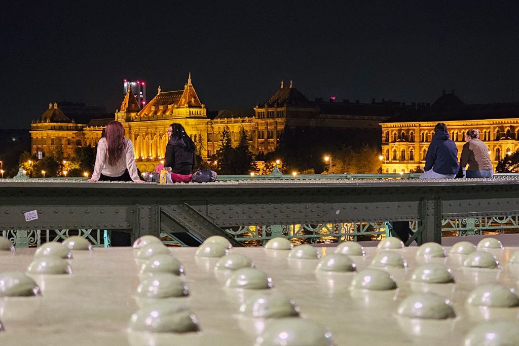 young people sitting on the railing of Liberty Bridge in Budapest at night