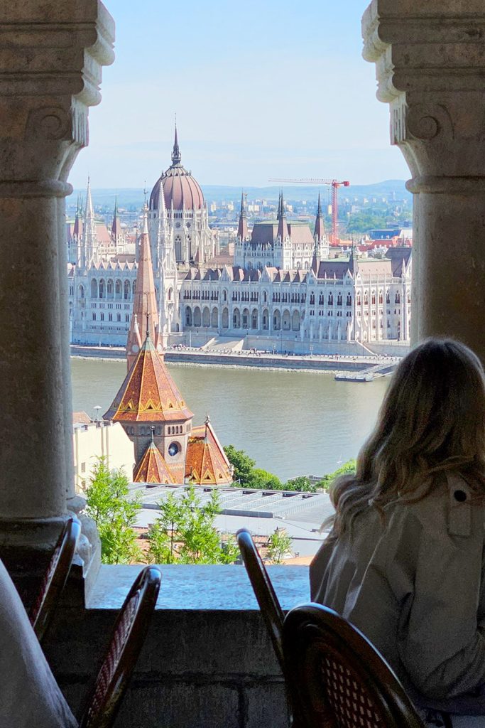 girl in a trench coat sitting in a cafe and enjoying the view of the Parliament