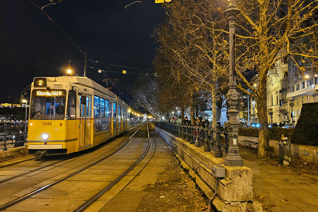 Yellow tram in Budapest on the Danube promenade on a crisp autumn night, with golden streetlights glowing through bare trees