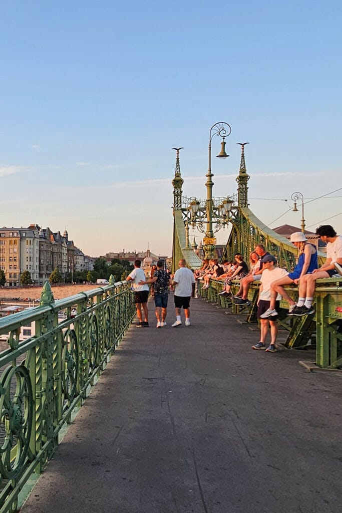 people sitting on the structure of Liberty Bridge and watching the sunset